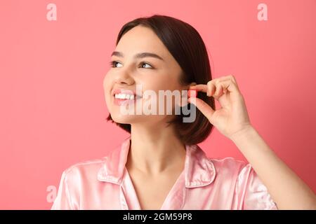 Jeune femme mettant le bouchon d'oreille sur fond rose Banque D'Images