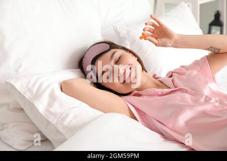 Jeune femme avec bouchon d'oreille dans le lit Banque D'Images