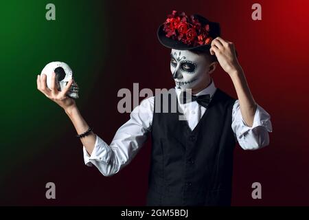Jeune homme au visage peint et au crâne de sucre pour la Journée des morts du Mexique (El Dia de Muertos) sur fond sombre Banque D'Images