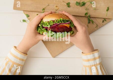 Femme tenant un savoureux hamburger végétarien sur fond de bois blanc Banque D'Images