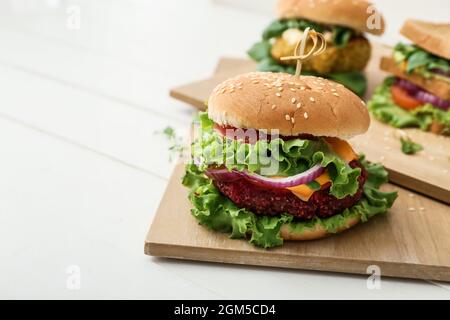 Planches en bois avec délicieux hamburgers végétariens sur fond de bois blanc Banque D'Images