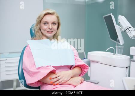 Charmante femme mûre assise dans une chaise dentaire, souriant à la caméra Banque D'Images