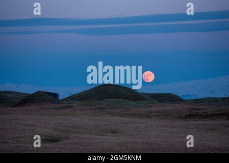 La pleine lune s'élève au-dessus du glacier islandais avec des collines ondulantes au premier plan Banque D'Images