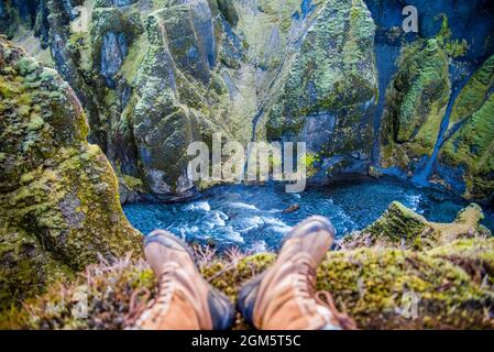 Canyon vert de la mousse d'Islande avec vues à couper le souffle. Vue sur les pieds des randonneurs avec des bottes donnant sur la rivière qui traverse le canyon. Banque D'Images