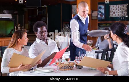 serveuse positive qui commande aux clients au café Banque D'Images