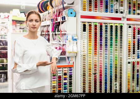 Jeune femme vendeuse de fournitures de couture magasin montrant