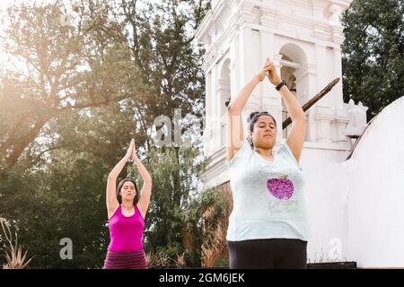 Jeunes femmes hispaniques faisant du yoga debout levant les armes à l'extérieur à Mexico Banque D'Images