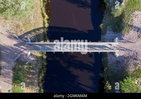 Un petit pont en bois traversant la rivière. Le soleil d'automne crée de longues ombres sur l'eau de la rivière. Banque D'Images