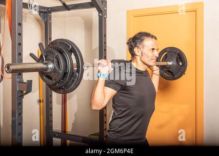 Gros plan sur un sportif qui fait des squats avec le bar de la salle de gym Banque D'Images