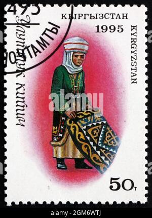 KIRGHIZISTAN - VERS 1995 : un timbre imprimé au Kirghizistan montre la femme en costume traditionnel kirghize avec tapis, vers 1995 Banque D'Images