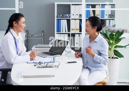 Femme vietnamienne mûre souriante répondant aux questions de son médecin lors d'une visite de contrôle annuelle Banque D'Images