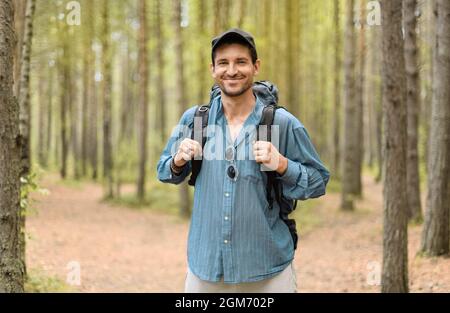 Homme souriant, 40 ans, avec son sac à dos touristique est debout dans une forêt. Banque D'Images