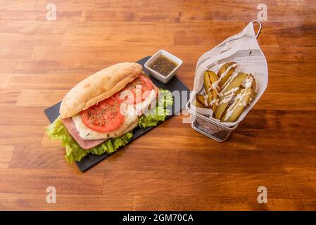 Sandwich de style milanais avec fromage fondu, tranches de tomate avec origan et jambon avec laitue sont sauce dans un bol blanc et garniture de pomme de terre sur la patte en bois Banque D'Images