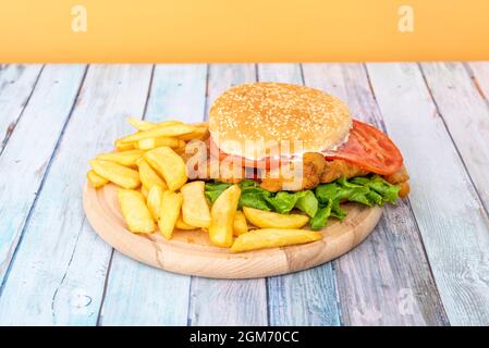 Sandwich milanais au poulet avec un pain hamburger et garniture de frites maison sur une assiette ronde en bois Banque D'Images