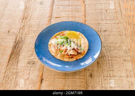 délicieux carnitas taco mexicain à la coriandre, compote de viande, oignon cru et coin de citron avec tortilla au blé et avocat bleu sur bois clair Banque D'Images