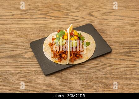 Tacos mexicains avec tortillas de blé avec guacamole, morceaux d'ananas et porc tiré sur plaque d'ardoise noire Banque D'Images