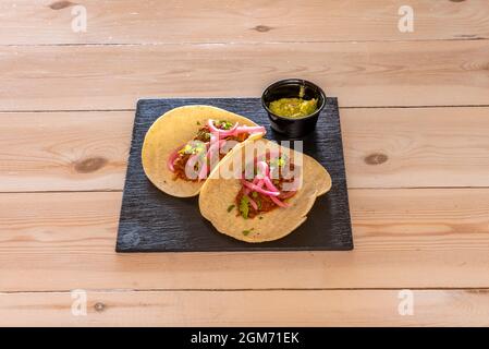 Deux tacos typiques de cochinita pibil mexicain avec guacamole dans un bol noir, oignon rouge, coriandre et ragoût de bœuf Banque D'Images