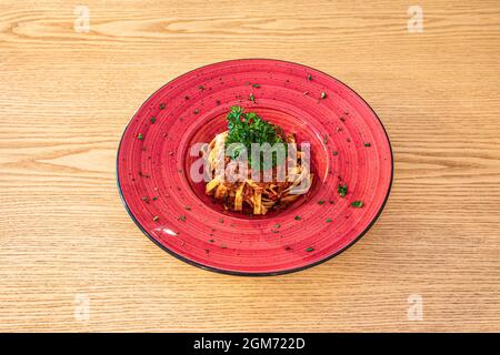 Jolie assiette rouge profond avec une recette servant de tagliatelle avec de la viande en sauce bolognaise. Banque D'Images