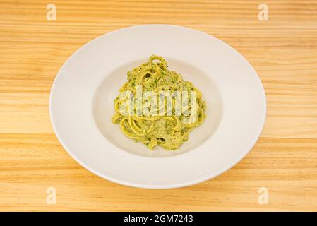 Recette italienne de pâtes tagliatelles avec sauce pesto et pistache sur plaque blanche et table en bois jaune Banque D'Images