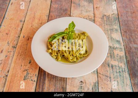 Tagliatelle de pâtes de légumes verts avec sauce au pesto italien, noix et feuilles de basilic sur une table en bois Banque D'Images