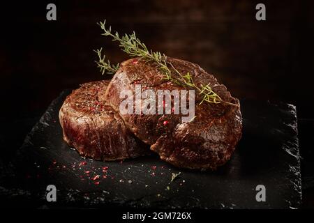 Délicieux filet mignon grillé aux assaisonnements servis sur une assiette noire sur fond sombre flou Banque D'Images