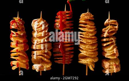 Vue de dessus avec de délicieuses pommes de terre tornado frites sur brochettes avec mayonnaise et ketchup sur fond noir Banque D'Images