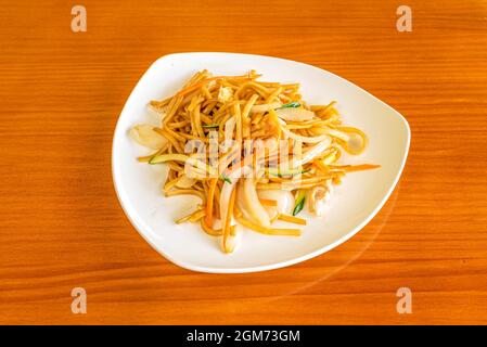 Assiette de nouilles sautées au wok trois spécialités chinoises au restaurant avec tables aux couleurs cerise Banque D'Images