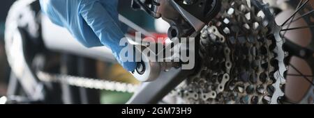 Un homme de main en gants de caoutchouc répare la bicyclette en atelier Banque D'Images