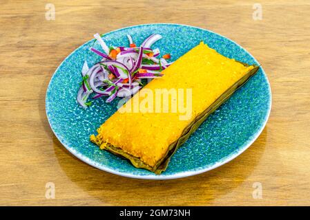 Tamale cuisiné dans un restaurant péruvien avec de l'oignon violet et du persil comme garniture Banque D'Images