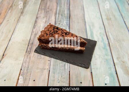 Portion de gâteau au chocolat noir avec deux couches de gâteau éponge et une de garniture sur une assiette en ardoise noire. Banque D'Images