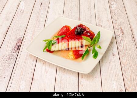 Cheesecake avec une merveilleuse garniture de fraise, baies et fraises hachées avec des feuilles de bonne herbe sur une table en bois clair. Banque D'Images