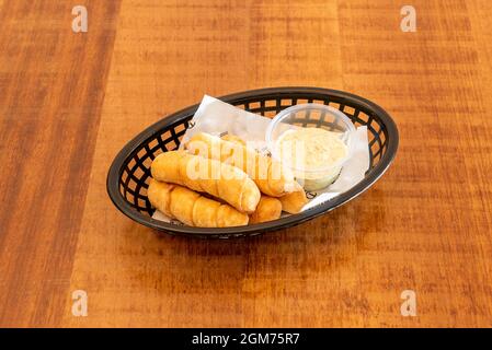 Plateau de tequeños vénézuélien farci de fromage avec sauce avocat et mayonnaise sur table en bois Banque D'Images