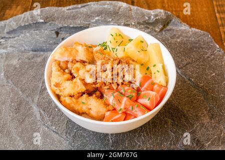 Bol avec saumon cru, morceaux d'ananas, légumes tempura et oignon frit avec ciboulette verte hachée Banque D'Images