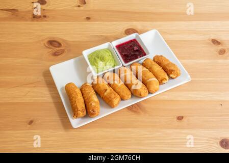 Assiette de tequeños vénézuélien fraîchement préparé avec deux sirops à tremper sur une table en pin Banque D'Images