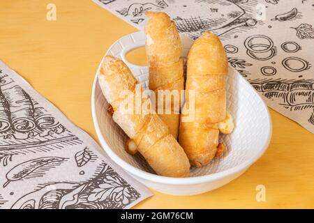 Image de plusieurs tequeños gras farcis avec beaucoup de fromage dans un joli bol blanc sur une table jaune Banque D'Images