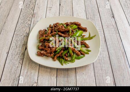 Recette typique de restaurant chinois avec des bandes de bœuf et de poivrons verts sautés sur une table en bois Banque D'Images