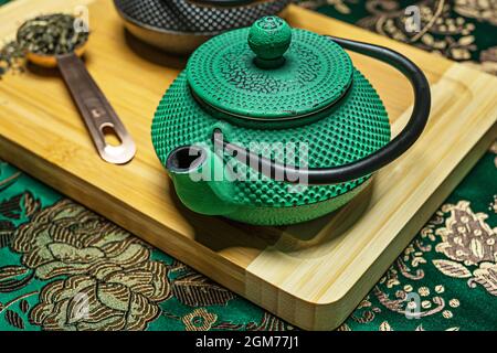 Gros plan de théière traditionnelle chinoise en fonte verte avec fond en tissu vert, casserole en cuivre avec thé sur table en bambou Banque D'Images