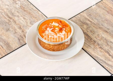Le curry de poulet tikka masala est servi dans un bol en métal traditionnel du restaurant pakistanais sur une table en marbre de différentes couleurs. Banque D'Images