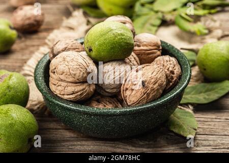 Noix mûres brunes et vertes non mûres dans un bol. Arrière-plan en bois ancien, gros plan Banque D'Images