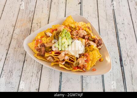 Nachos de maïs au guacamole, fromage à la crème, compote de poulet, jalapeno en tranches, maïs doux et pico de gallo sur table blanche Banque D'Images