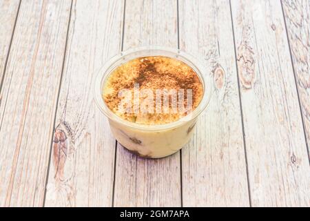 Dessert tiramisu individuel avec cannelle et chocolat en poudre à l'intérieur d'un récipient de livraison à la maison sur une table en bois Banque D'Images