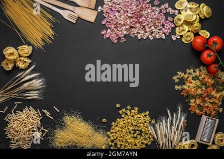 composition avec de nombreuses sortes de pâtes, tomates et ustensiles de cuisine sur fond noir Banque D'Images