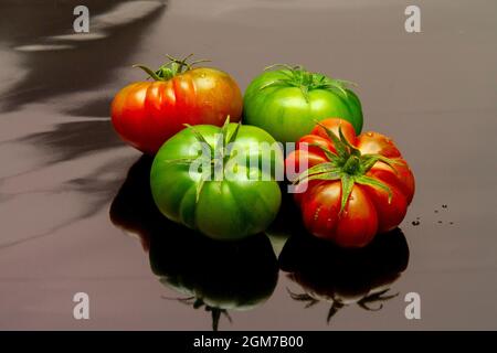 tomates raf mûres et vertes sur surface noire réfléchissante Banque D'Images