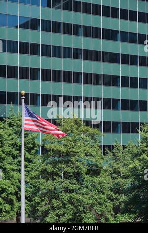 Arbres et drapeau américain volant sur un mât devant un immeuble de bureaux en verre moderne vert du milieu du siècle à Rosslyn, en Virginie, près de Washington DC. Banque D'Images