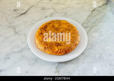 Omelette espagnole avec beaucoup de jus servie sur une assiette blanche sur une table en marbre blanc Banque D'Images