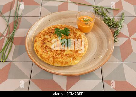 Omelette espagnole pour une personne avec un côté de salmorejo, avec romarin, ciboulette et persil Banque D'Images