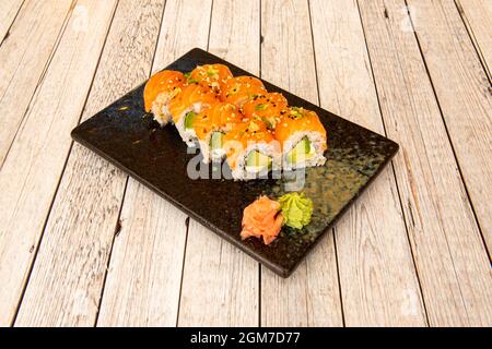 Rouette de sushi uramaki recouverte de saumon norvégien et farcie d'algues nori, de fromage à la crème et d'avocat mûr avec wasabi et ginseng avec sésame et p Banque D'Images