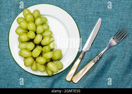 Raisins blancs dessert sur plaque métallique émaillée avec rebord vert et couverts vintage sur tissu bleu Banque D'Images