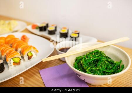 Bol de salade wakame avec baguettes en bois et makis et uramaki en arrière-plan sur la table d'un restaurant asiatique Banque D'Images