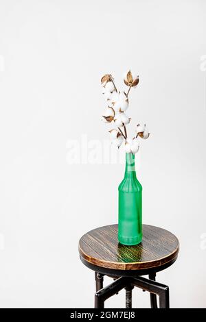 Vase décoratif avec branche de coton sur tabouret en bois et en métal avec fond blanc. Banque D'Images